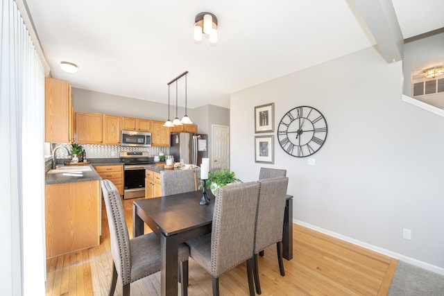 dining space featuring light wood finished floors, beamed ceiling, and baseboards