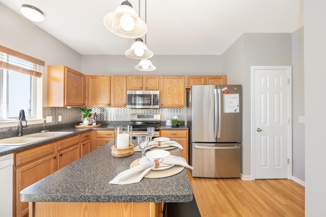 kitchen with stainless steel appliances, dark countertops, hanging light fixtures, a sink, and a kitchen island