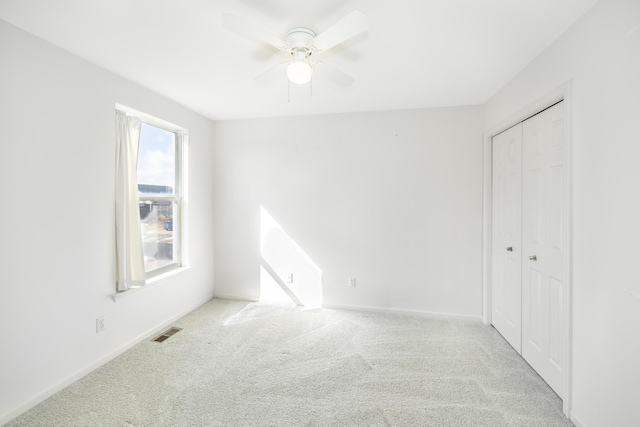 unfurnished bedroom featuring a closet, visible vents, a ceiling fan, light carpet, and baseboards