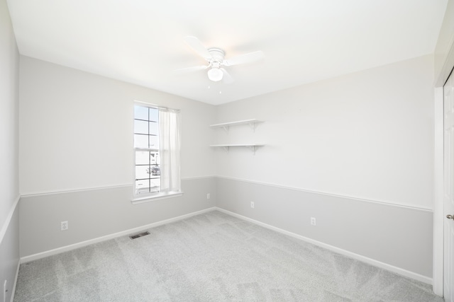 carpeted empty room with baseboards, visible vents, and a ceiling fan