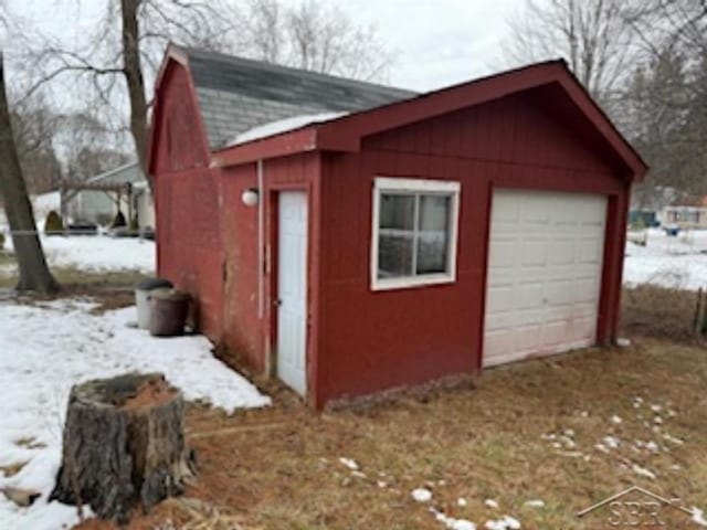 snow covered structure with driveway and an outdoor structure