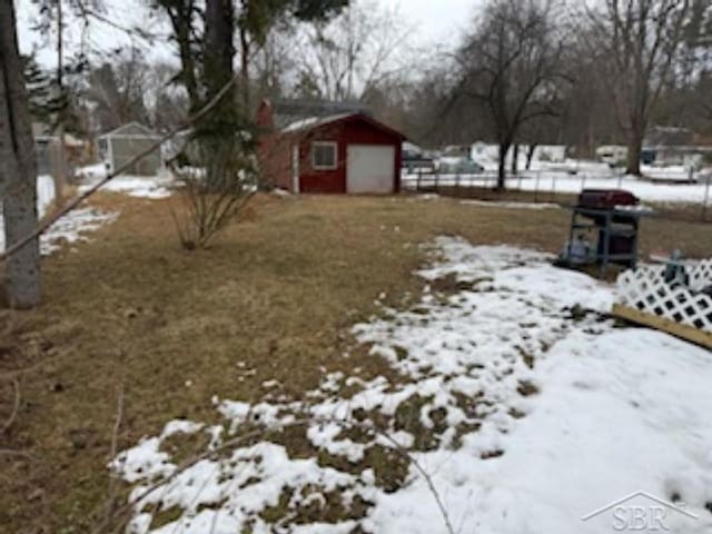 snowy yard with a garage and an outbuilding