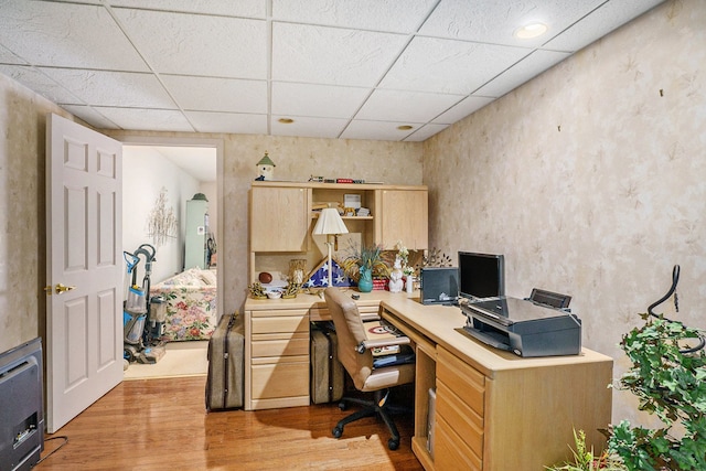 office space with light wood finished floors, arched walkways, and a drop ceiling