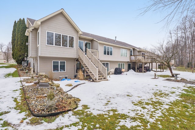 snow covered back of property with a wooden deck and stairs