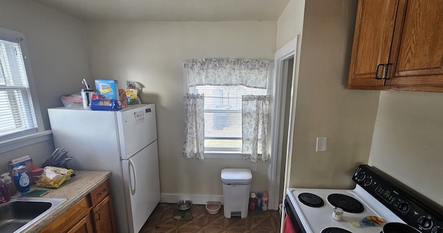 kitchen with freestanding refrigerator, brown cabinetry, a sink, and range with electric stovetop