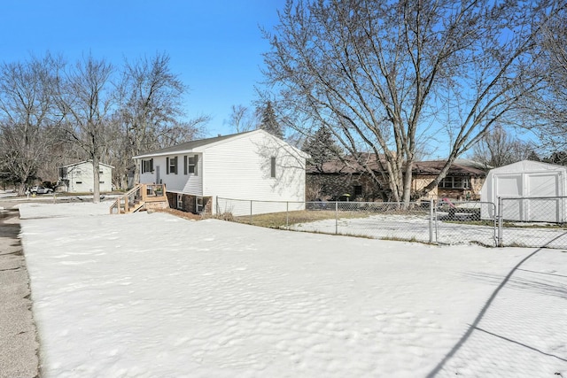 snow covered property with a garage, a residential view, fence, and a storage shed