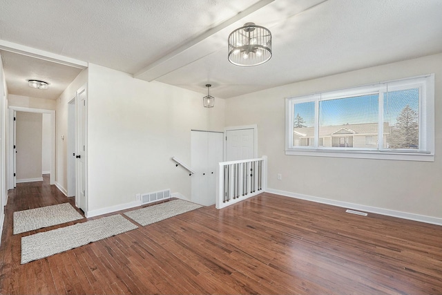 empty room with dark wood-style floors, a textured ceiling, visible vents, and baseboards