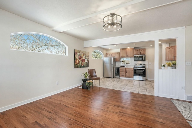 living room with a notable chandelier, light wood finished floors, beverage cooler, beamed ceiling, and baseboards