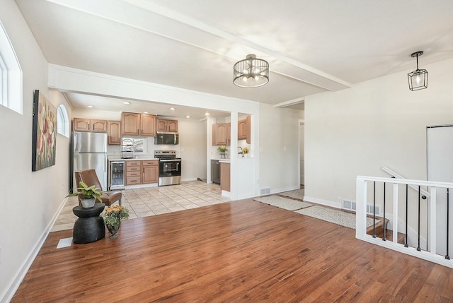 unfurnished living room with wine cooler, visible vents, an inviting chandelier, light wood-style floors, and baseboards