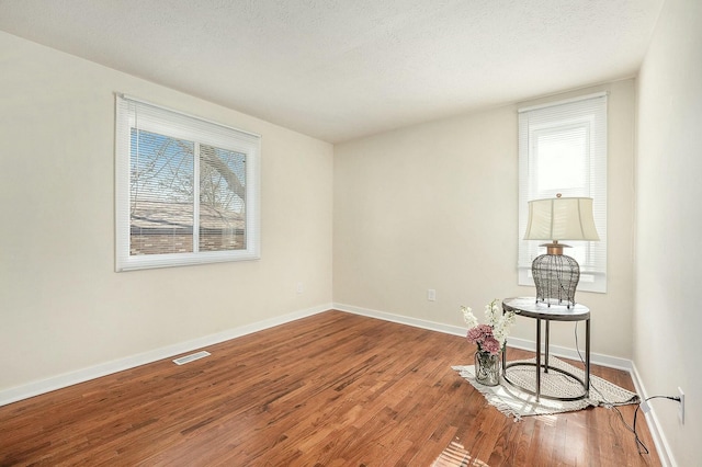 empty room featuring a healthy amount of sunlight, a textured ceiling, baseboards, and wood finished floors