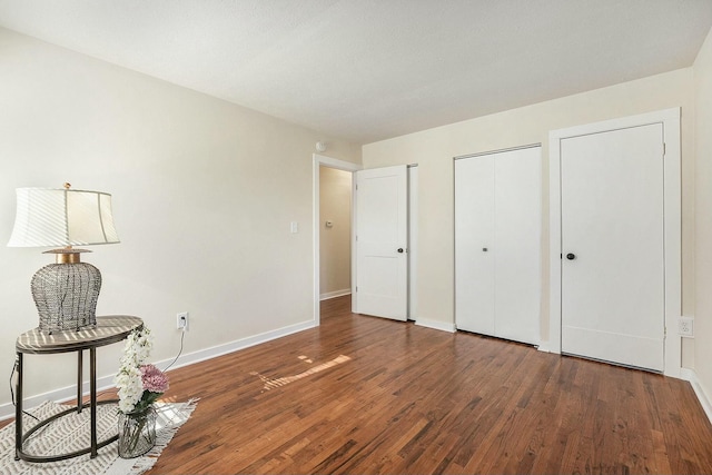 bedroom featuring dark wood-style floors, baseboards, and multiple closets