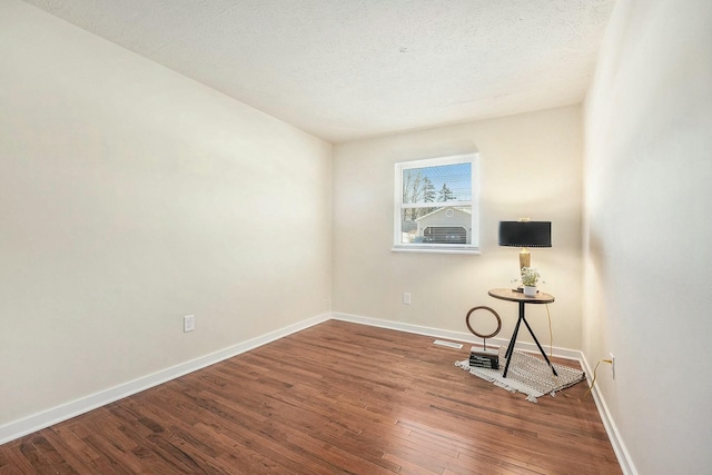 unfurnished room with wood-type flooring, visible vents, baseboards, and a textured ceiling