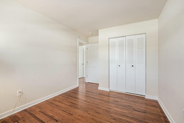 unfurnished bedroom featuring dark wood-type flooring, a closet, and baseboards