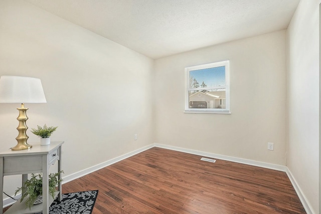 unfurnished room with visible vents, a textured ceiling, baseboards, and wood finished floors