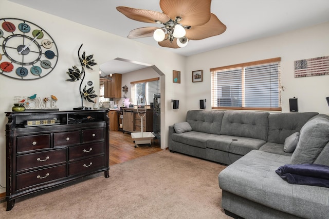 living room with arched walkways, ceiling fan, and light carpet