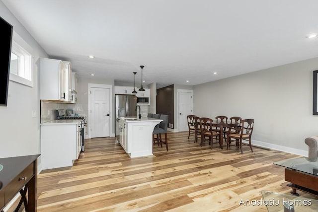 kitchen with a kitchen island with sink, stainless steel appliances, light countertops, white cabinetry, and pendant lighting