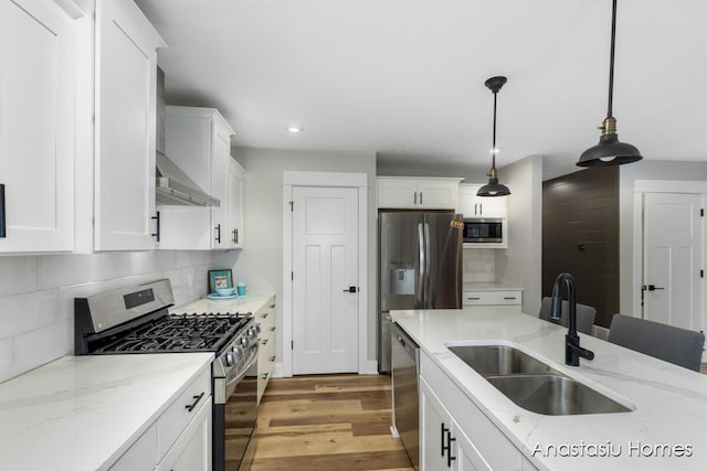 kitchen with light stone counters, stainless steel appliances, hanging light fixtures, white cabinetry, and a sink