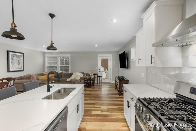 kitchen with white cabinets, appliances with stainless steel finishes, open floor plan, wall chimney range hood, and a sink