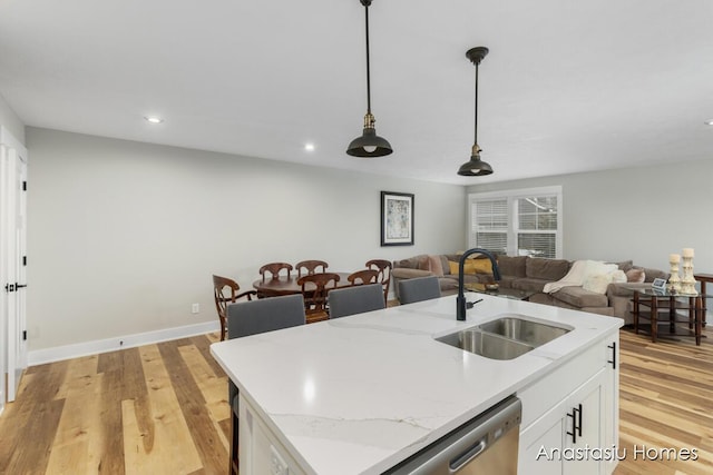 kitchen with a kitchen island with sink, a sink, white cabinetry, open floor plan, and pendant lighting