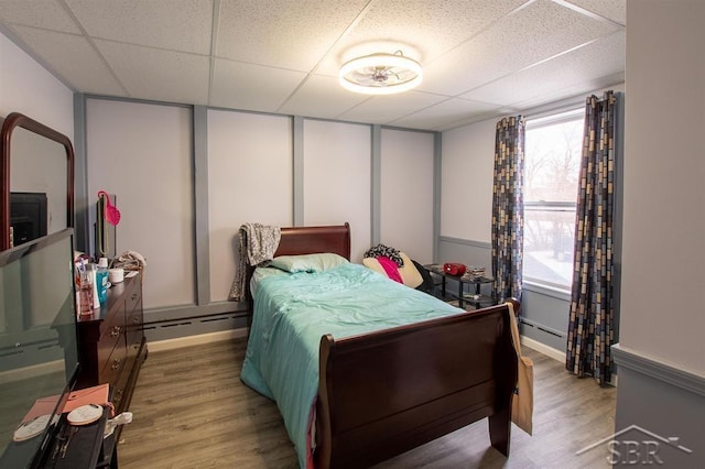 bedroom featuring a paneled ceiling, baseboard heating, and wood finished floors