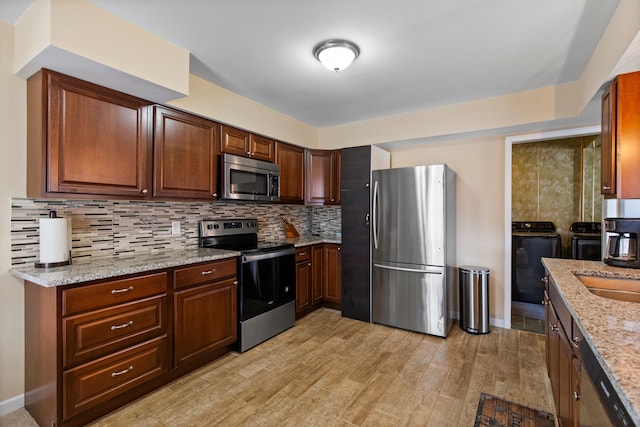 kitchen with appliances with stainless steel finishes, backsplash, washer and clothes dryer, and light stone counters