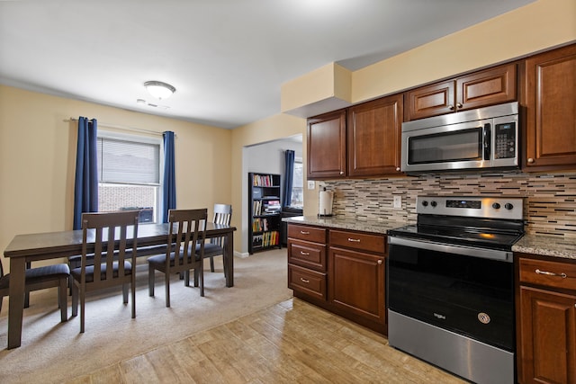 kitchen featuring light stone counters, stainless steel appliances, baseboards, light wood-type flooring, and decorative backsplash