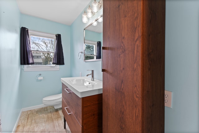 half bathroom with baseboards, vanity, toilet, and wood finished floors