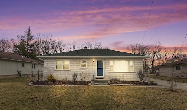 view of front of house with brick siding, roof with shingles, a chimney, entry steps, and a front lawn