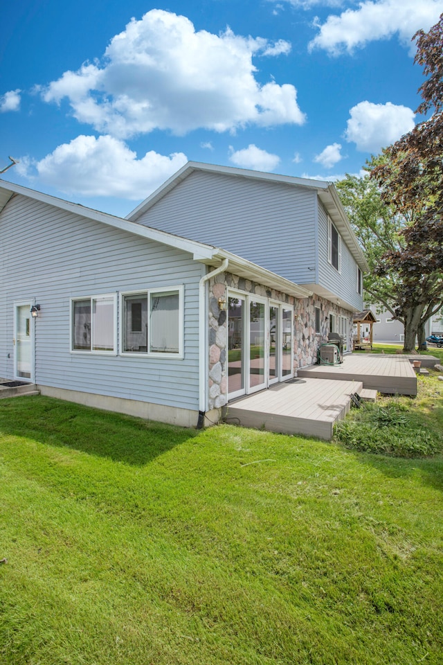 back of house featuring a yard, stone siding, and a wooden deck