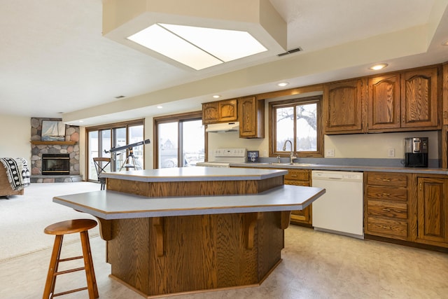 kitchen with brown cabinets, a breakfast bar area, visible vents, open floor plan, and white appliances