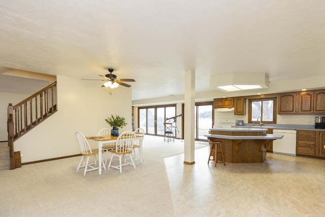 kitchen featuring white dishwasher, a breakfast bar, a kitchen island, light countertops, and brown cabinets