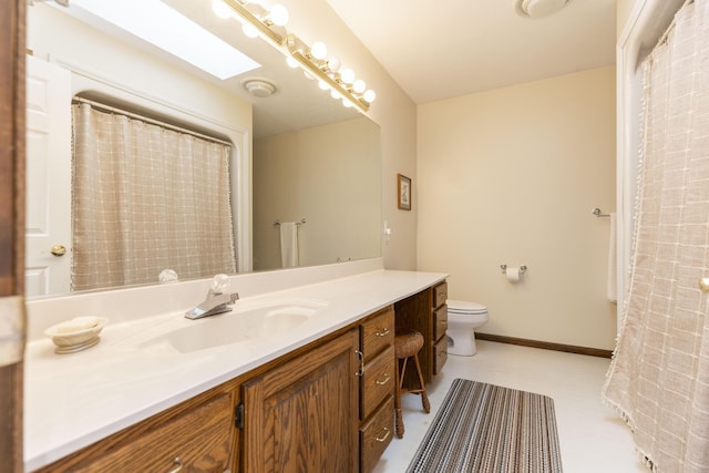 bathroom with a skylight, toilet, vanity, and baseboards