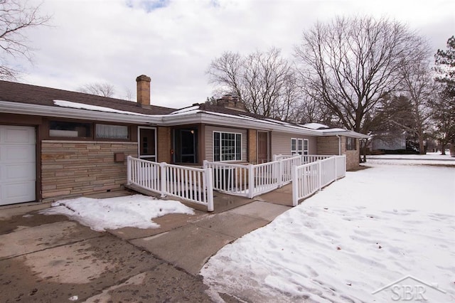 ranch-style house with a garage, covered porch, and a chimney