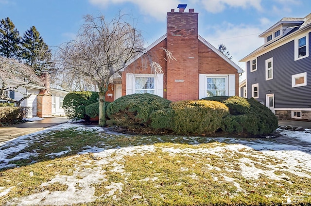 view of snowy exterior featuring brick siding, a chimney, and a lawn