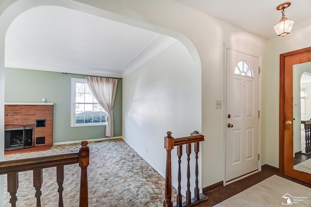 foyer featuring arched walkways, a brick fireplace, and baseboards