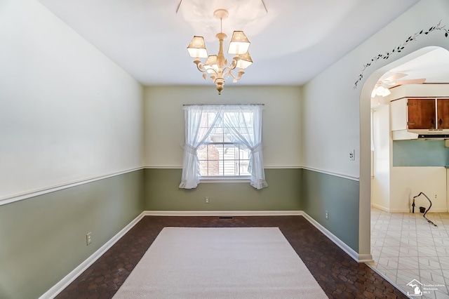 unfurnished dining area featuring arched walkways, a chandelier, and baseboards