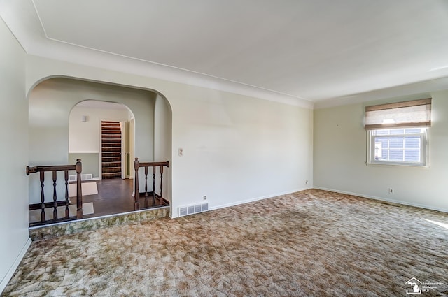 spare room featuring arched walkways, dark colored carpet, visible vents, stairway, and baseboards