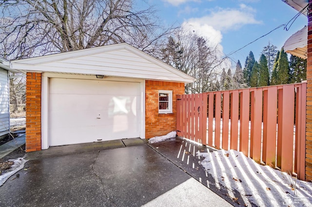 snow covered garage with driveway, a detached garage, and fence