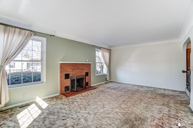 unfurnished living room with visible vents, arched walkways, baseboards, carpet floors, and a brick fireplace