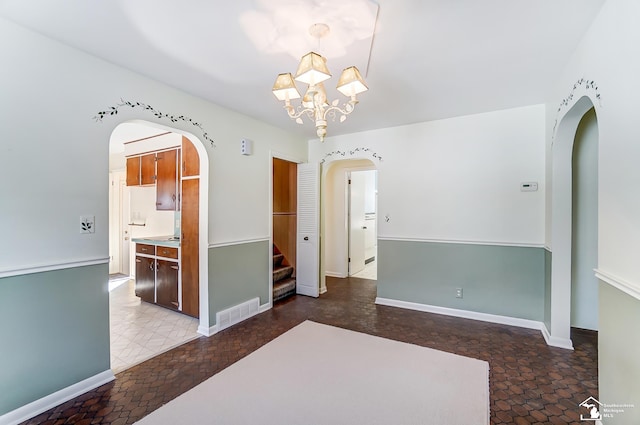 spare room featuring arched walkways, baseboards, visible vents, and an inviting chandelier