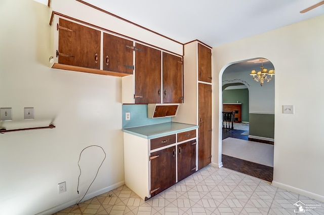 kitchen with arched walkways, a fireplace, baseboards, light countertops, and hanging light fixtures