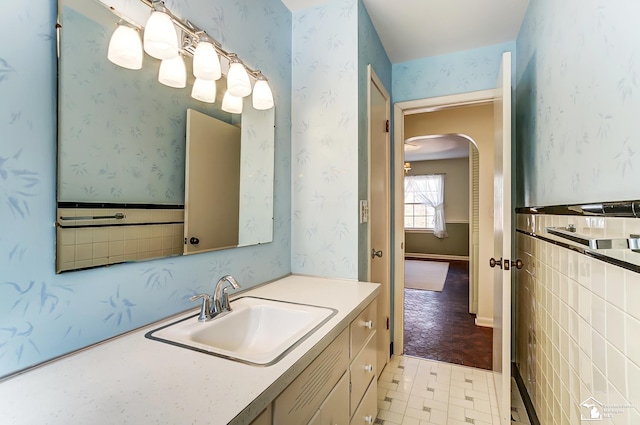 bathroom with wallpapered walls, vanity, and wainscoting