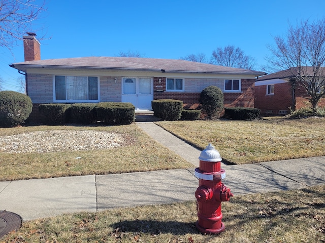 ranch-style house featuring brick siding, a chimney, and a front lawn