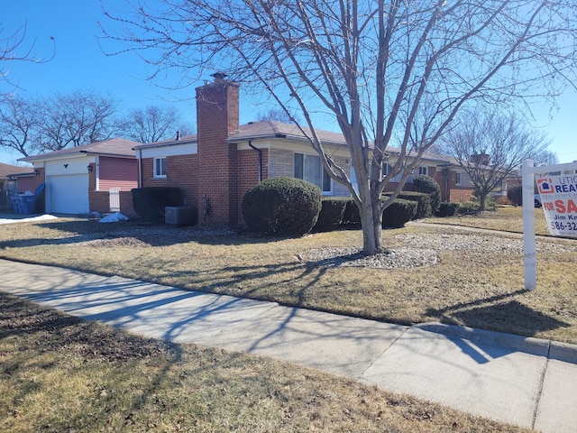 view of front of house with brick siding, a chimney, an attached garage, and cooling unit