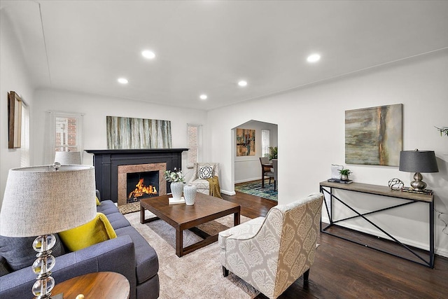 living area featuring arched walkways, a lit fireplace, wood finished floors, and recessed lighting