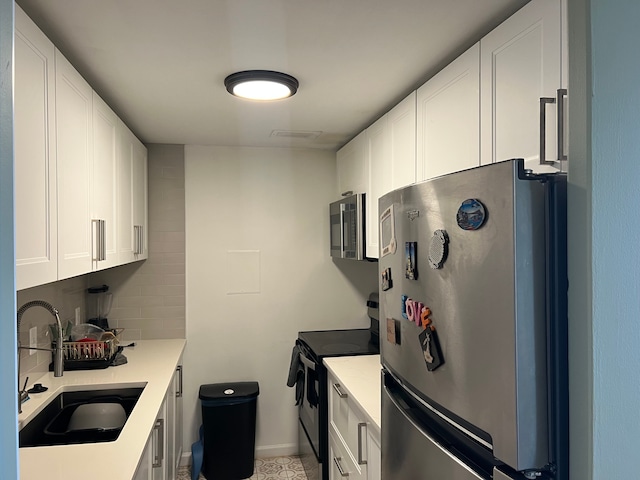 kitchen featuring black electric range, a sink, freestanding refrigerator, and white cabinets