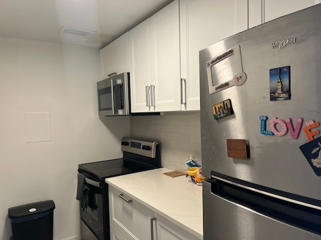 kitchen with stainless steel appliances, visible vents, white cabinetry, backsplash, and light stone countertops