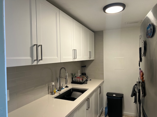 kitchen featuring tasteful backsplash, refrigerator, light countertops, white cabinetry, and a sink