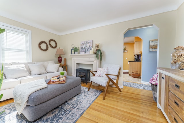 living area with arched walkways, baseboards, and light wood finished floors