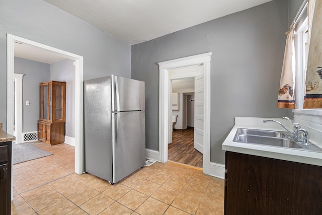 kitchen with light tile patterned floors, dark brown cabinetry, a sink, light countertops, and freestanding refrigerator